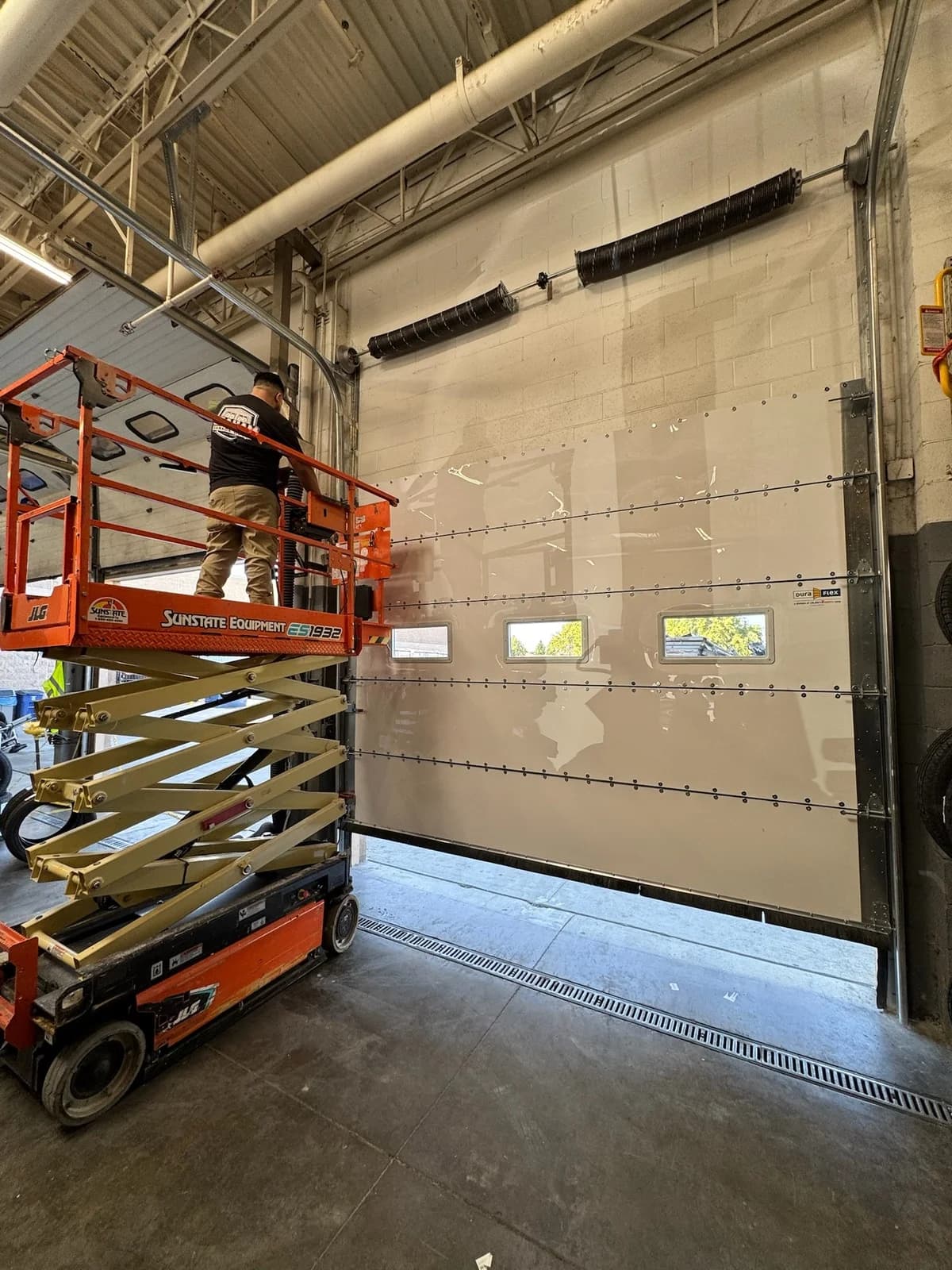 Technician servicing a commercial sectional garage door from a scissor lift in Sacramento
